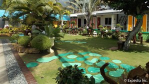 A courtyard with palm trees, potted plants, and a building with a blue roof. - L&M Hearthstones Lodge (Oslob)