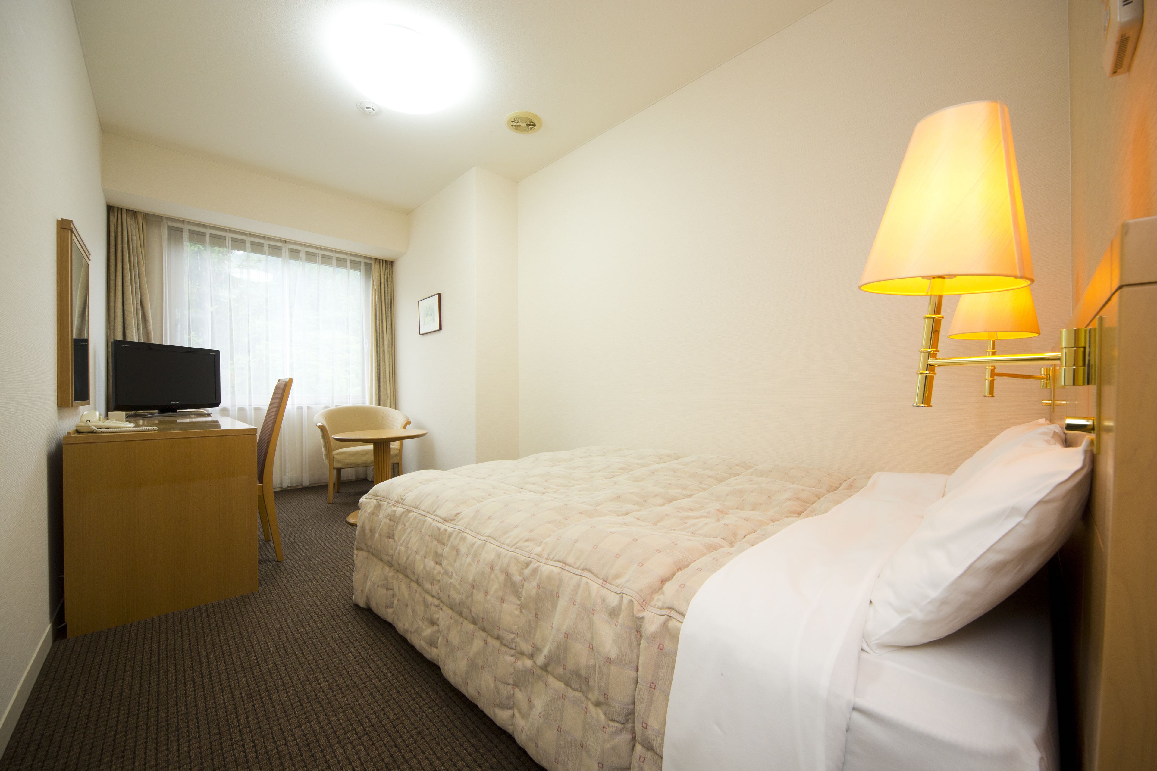 Ett hotellrum med en säng, ett skrivbord med en tv, en stol och en lampa.