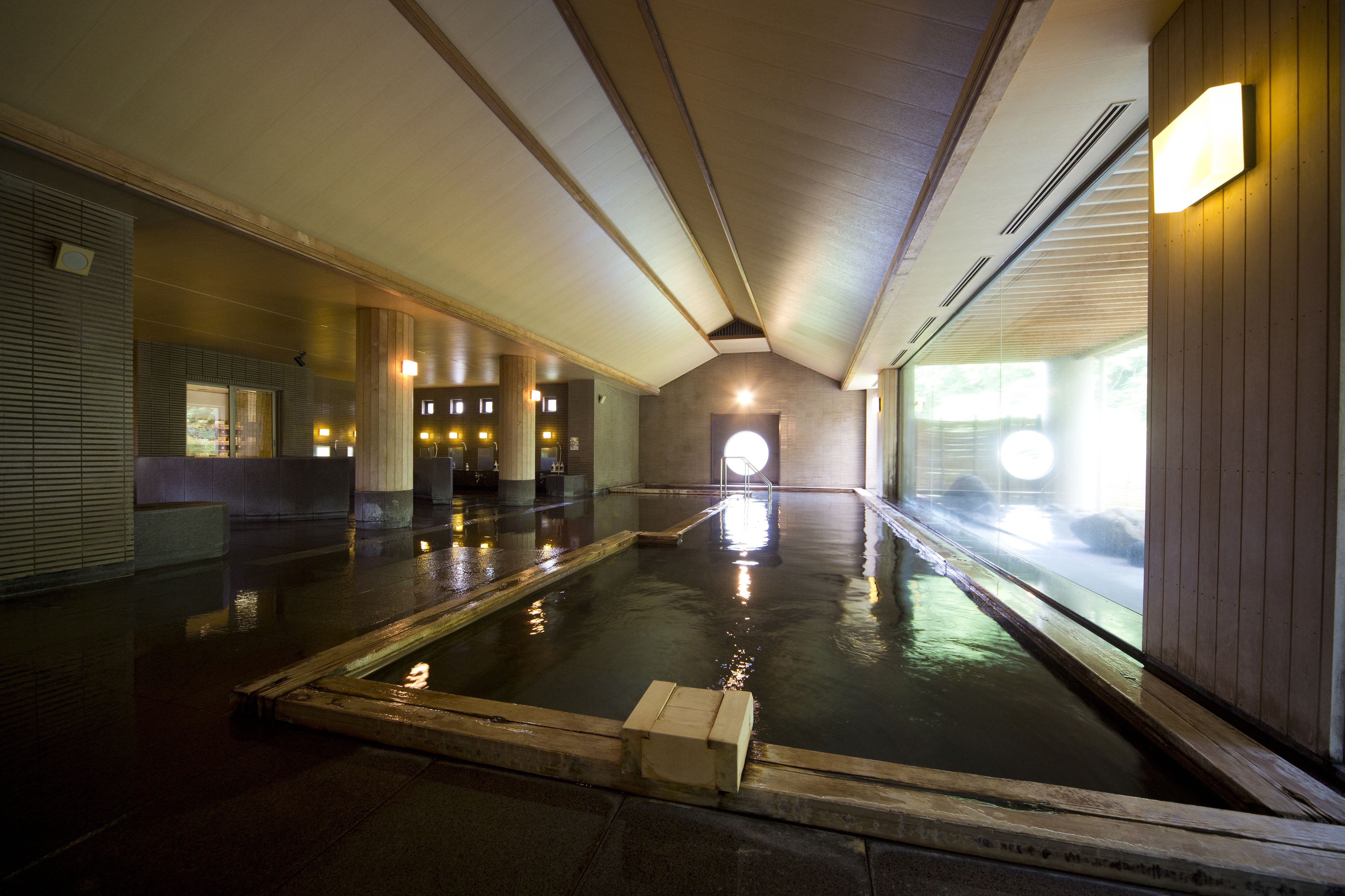 A traditional Japanese onsen with a wooden interior, a hot spring bath, and a view of the outdoors.