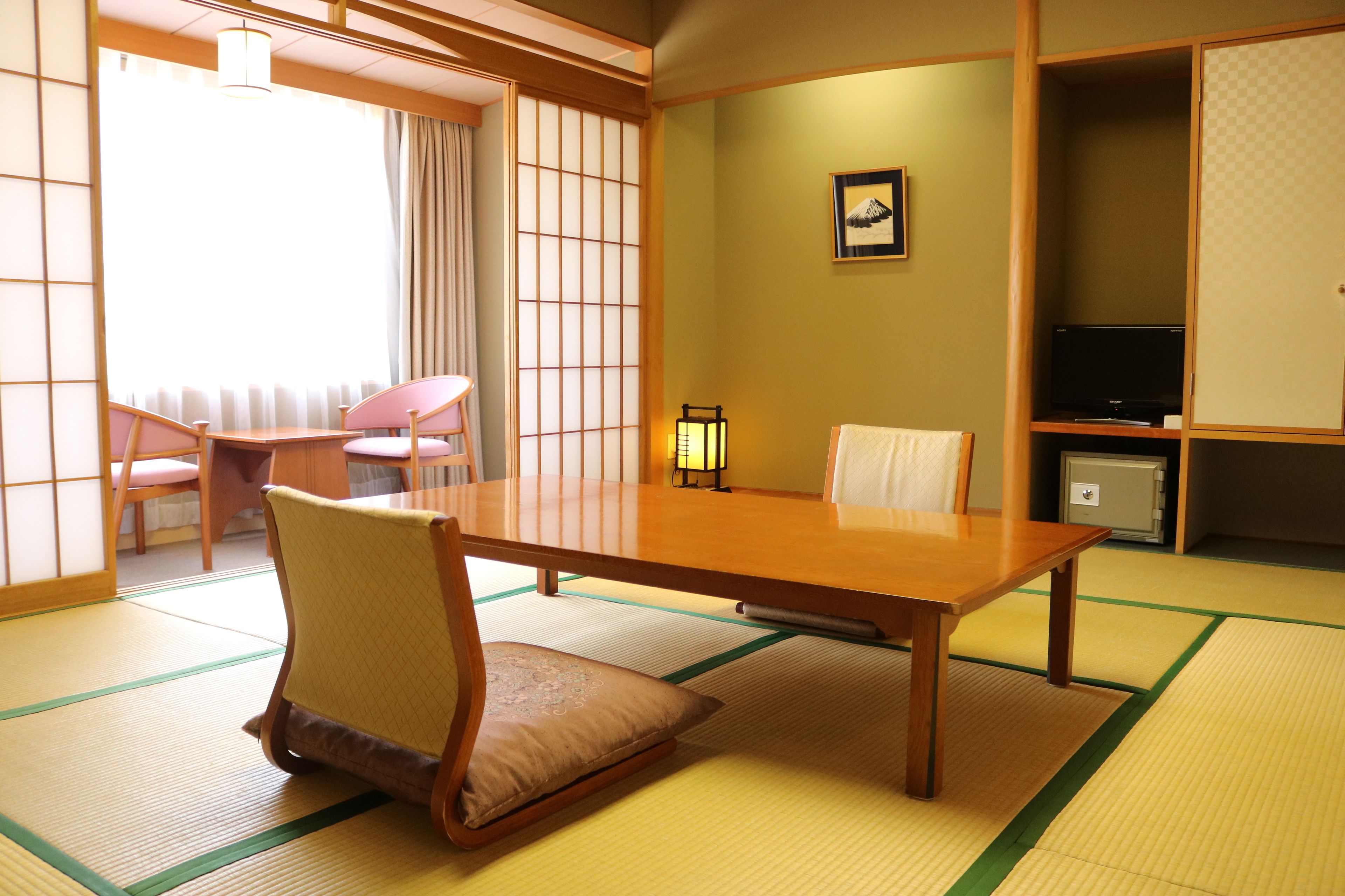Una habitación tradicional japonesa con suelo de tatami, una mesa baja, sillas, un televisor y un mueble pequeño.