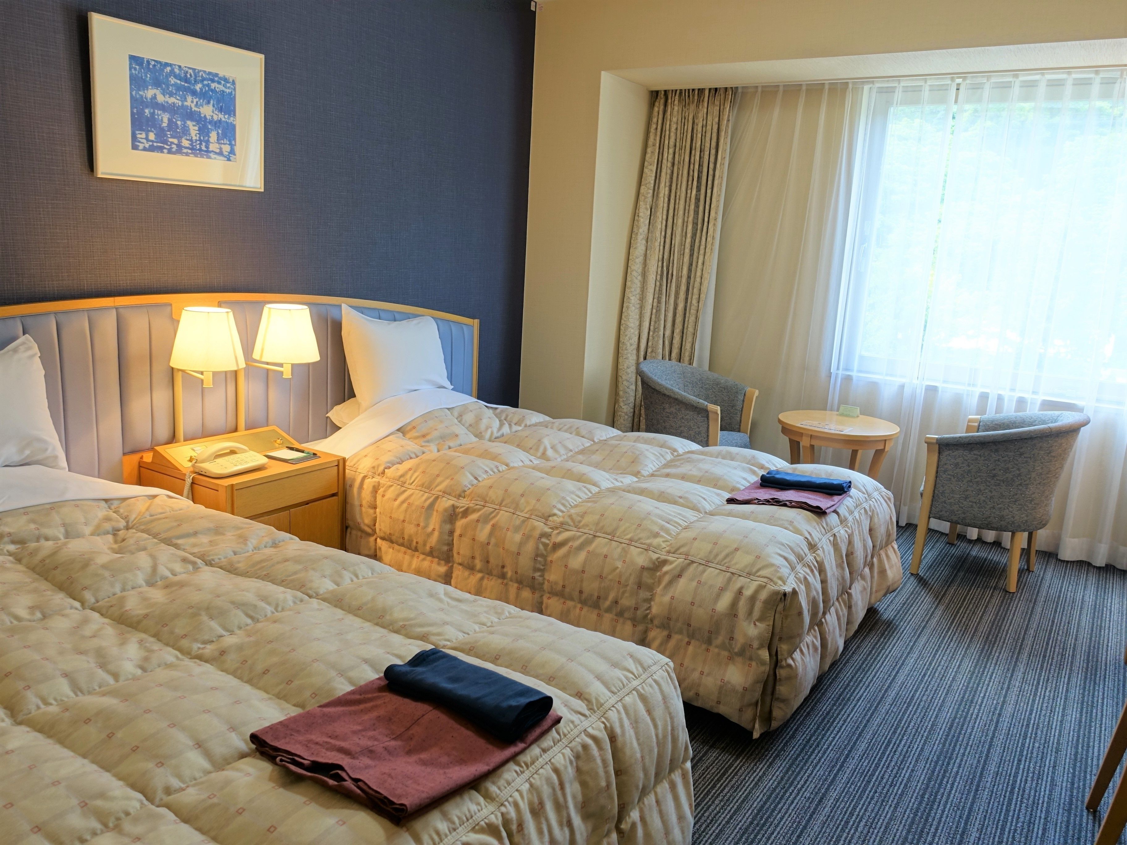 Une chambre d’hôtel avec deux lits, un bureau, une chaise et une petite table.