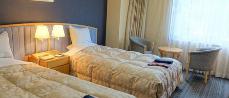 A hotel room with two beds, a desk, a chair, and a small table.