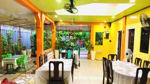 Un restaurante con varias mesas y sillas, plantas de interior y un ventilador de techo.