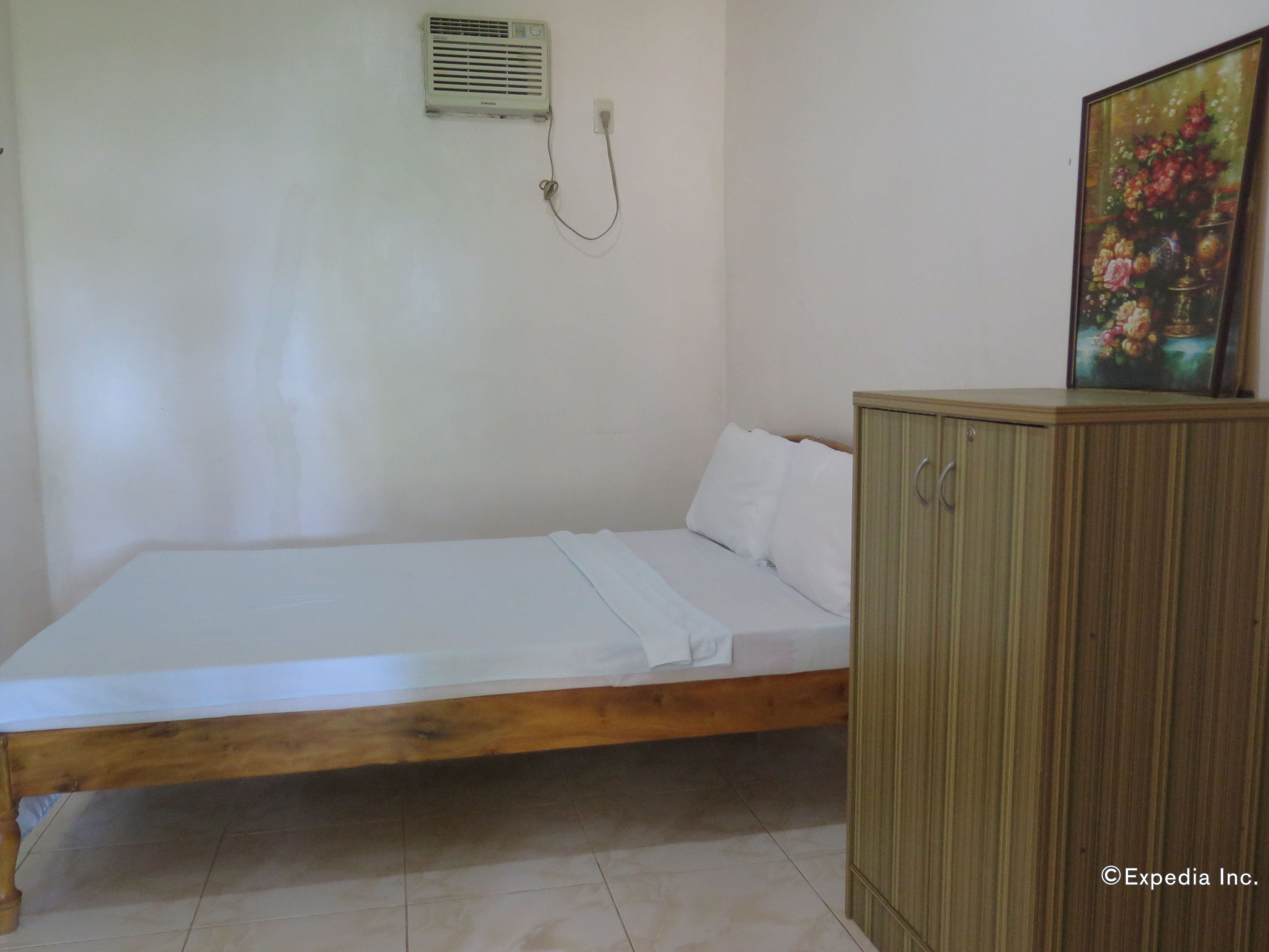 Una habitación sencilla con una cama de madera, un equipo de aire acondicionado pequeño y un armario con un cuadro.