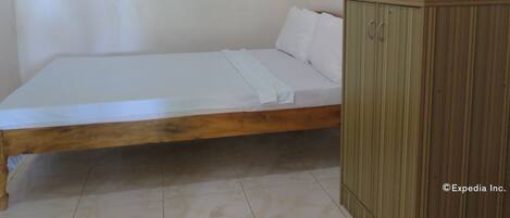Una habitación sencilla con una cama de madera, un equipo de aire acondicionado pequeño y un armario con un cuadro.