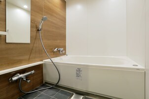 Un baño moderno con una bañera blanca, un cabezal de ducha de mano y un inodoro integrado.