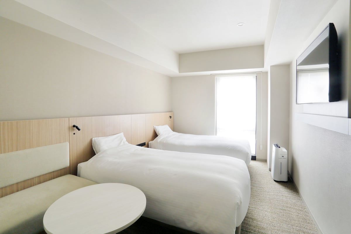 A hotel room with two beds, a round table, a flat-screen TV, and a window.