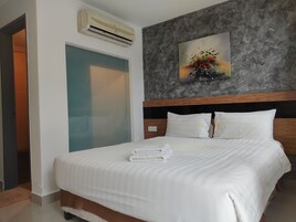 A hotel room with a bed, white bedding, a painting on the wall, and an air conditioning unit.