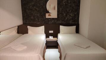 Habitación de hotel con dos camas, una mesita de noche, un teléfono y una lámpara fijada a la pared.