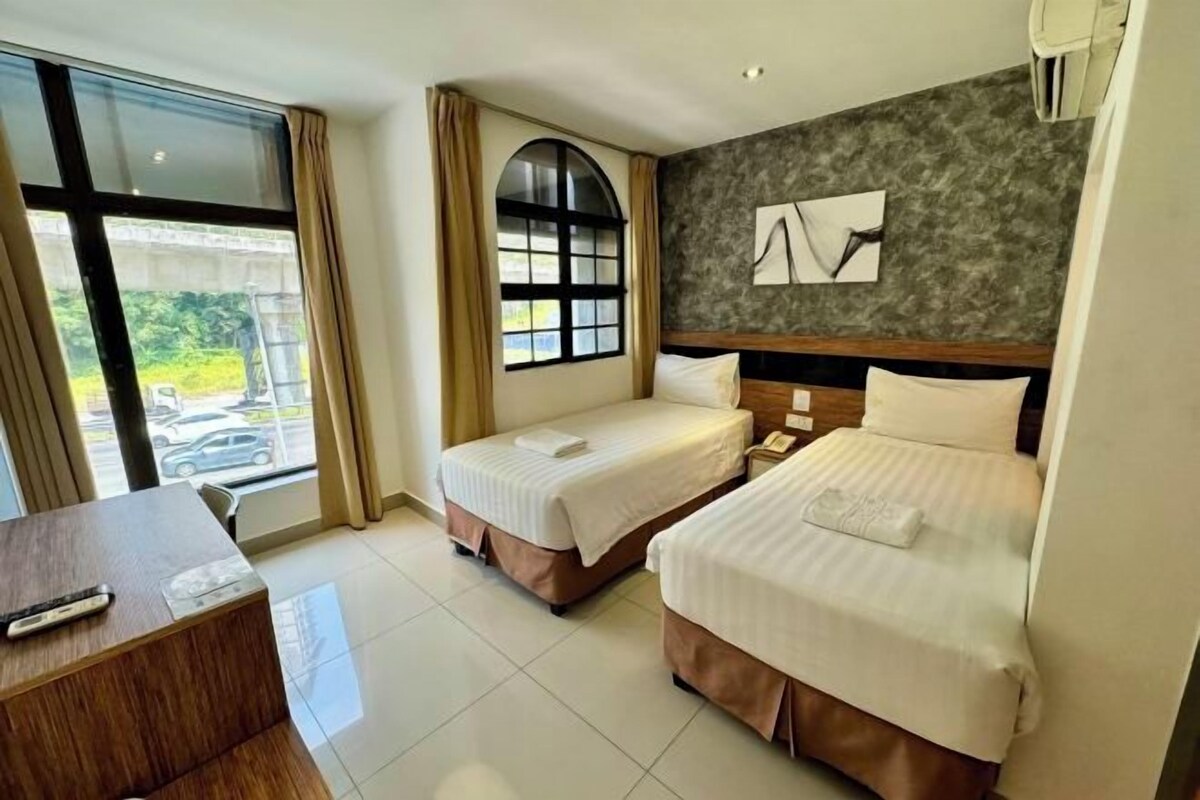 A hotel room with two beds, a desk, a large window, and a view of the outside.
