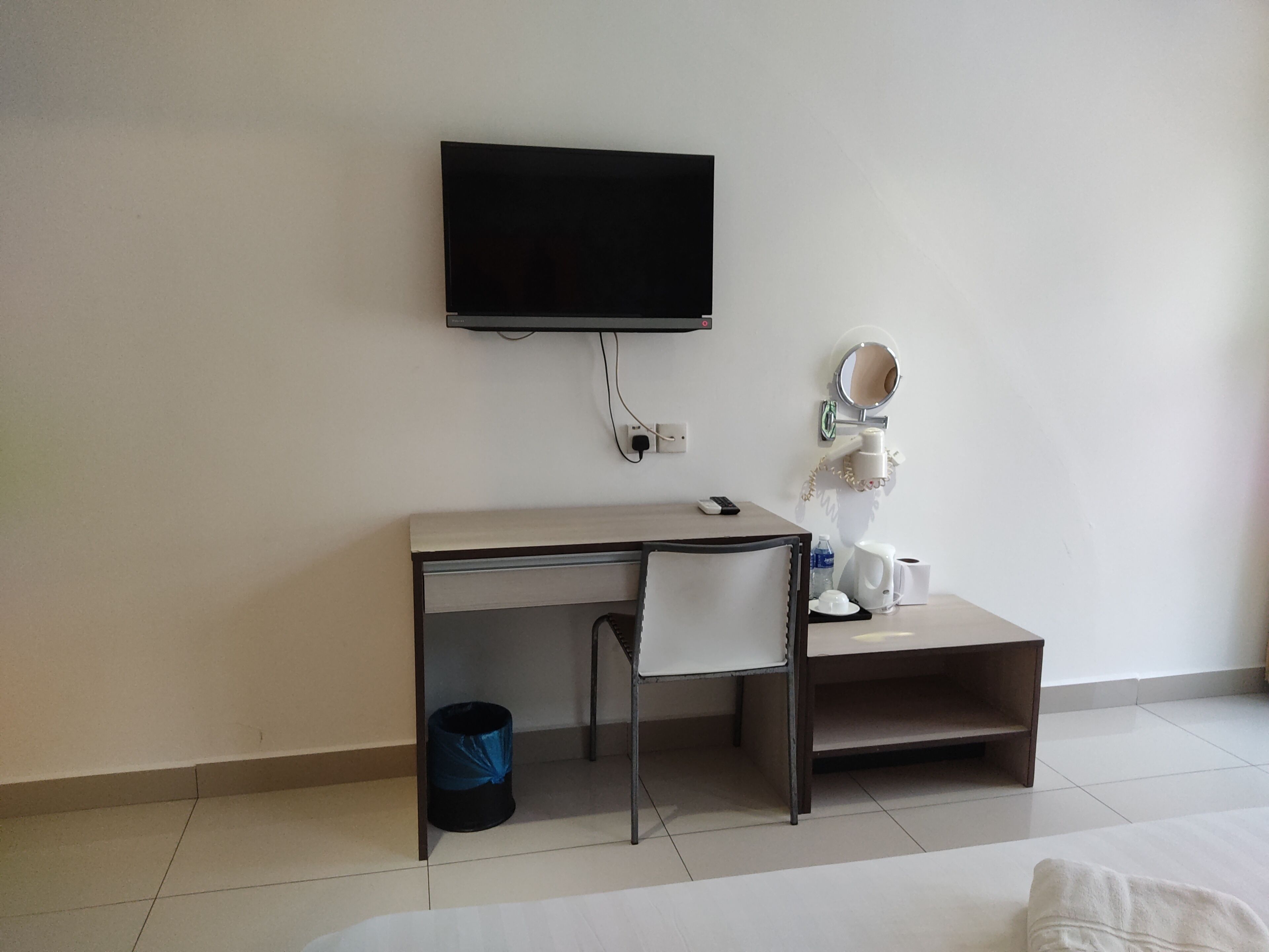 A hotel room with a desk, a television, a mirror, a trash bin, and a bed.