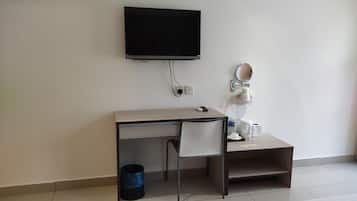 A hotel room with a desk, a television, a mirror, a trash bin, and a bed.