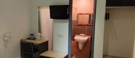 A hotel room with a bed, a small bedside table, a wall-mounted TV, a bathroom with a sink and mirror, and an air conditioning unit.