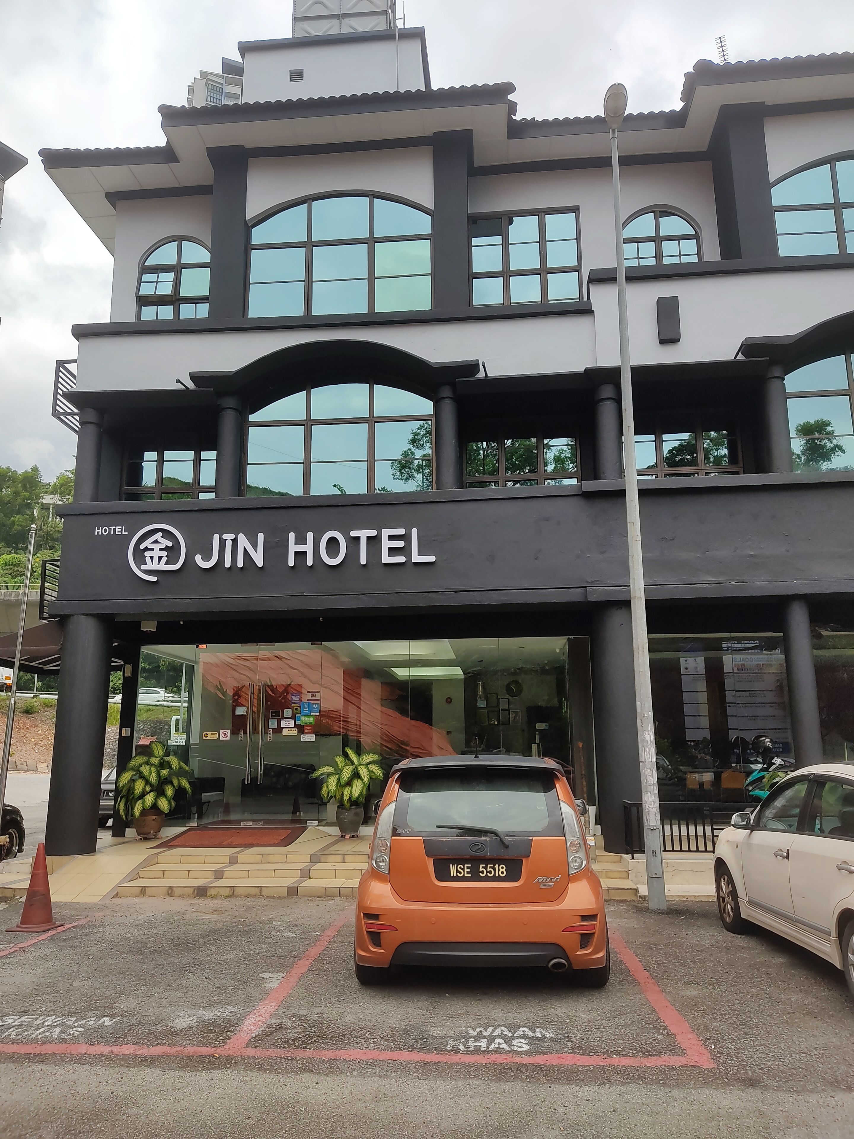 Un Hotel Jin de dos pisos con fachada moderna, ventanas grandes y un estacionamiento con dos coches.