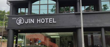 Un Hotel Jin de dos pisos con fachada moderna, ventanas grandes y un estacionamiento con dos coches.