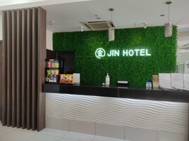 A hotel reception desk with a green wall, a modern design, and a sign that reads "JIN HOTEL".