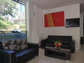 A modern living room with a black sofa, a coffee table with a vase of flowers, a red abstract painting, and a TV mounted on the wall.