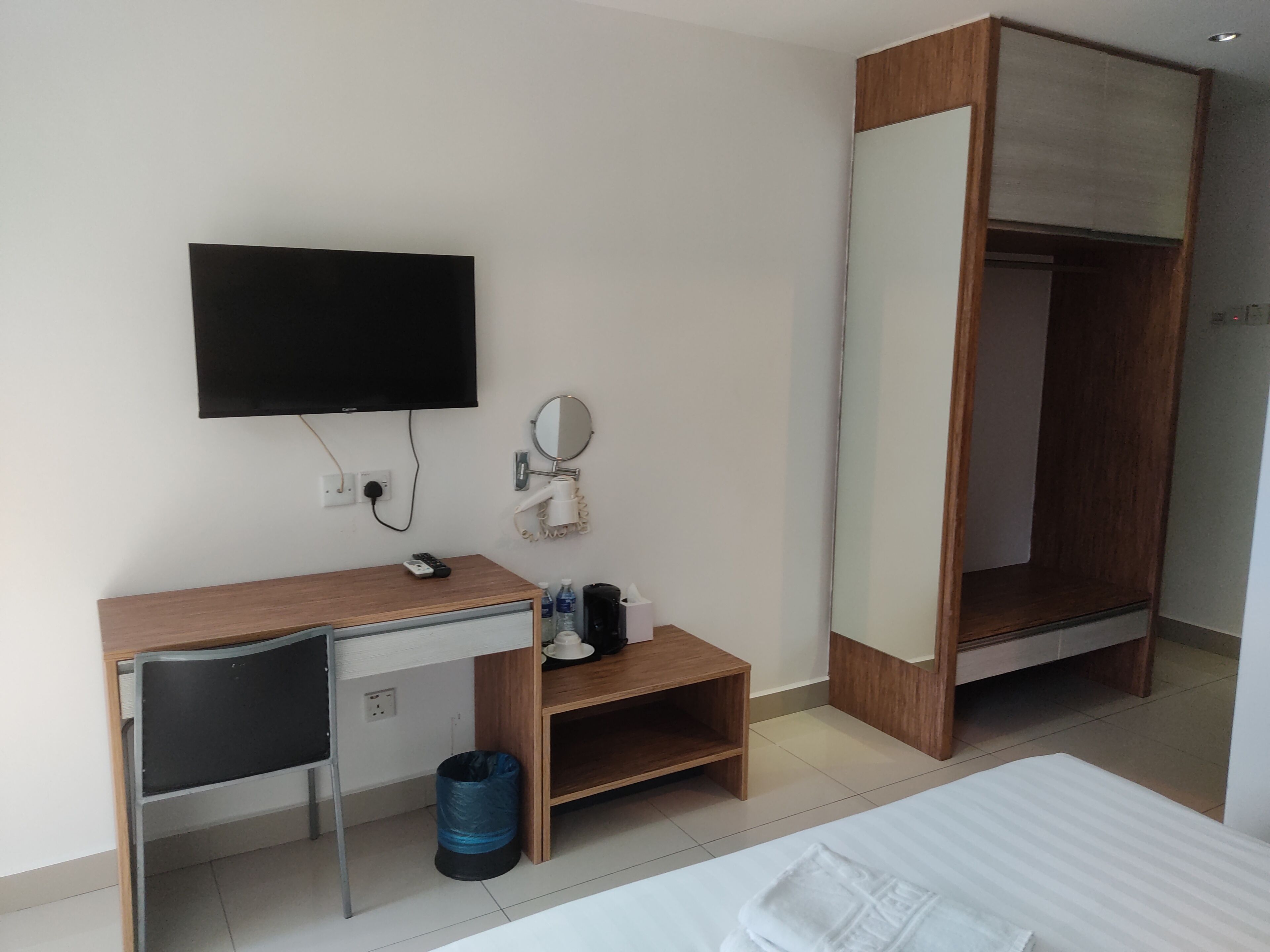 Ein Hotelzimmer mit einem Holztisch, einem Fernseher, einem Spiegel, einem Kleiderschrank und einem Bett.