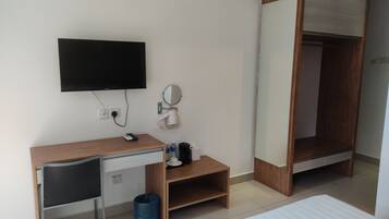 Quarto de hotel com escrivaninha de madeira, televisão, espelho, guarda-roupa e cama.