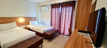 Una habitación de hotel con dos camas, un escritorio de madera, un televisor y una ventana con cortinas.