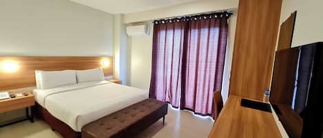 Habitación de hotel con cama, mesita de noche, banco, televisión y cortinas.