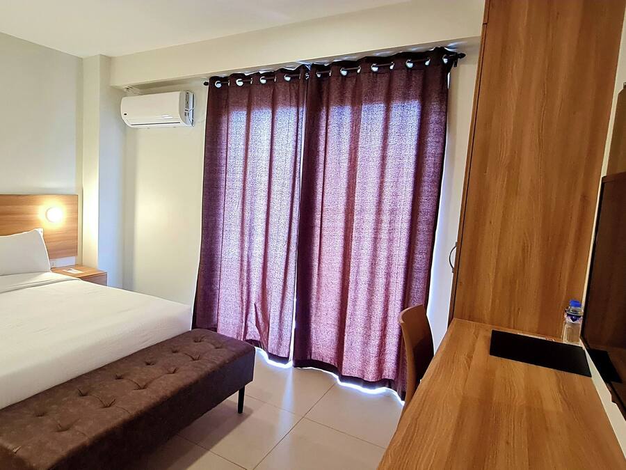 A hotel room with a bed, bedside table, bench, TV, and curtains.