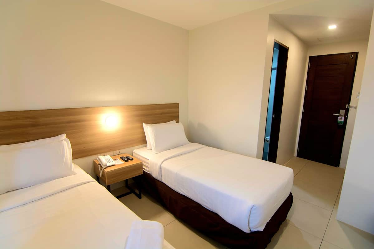 Quarto de hotel com duas camas, um painel de cabeceira de madeira, mesa de cabeceira com telefone e uma porta.