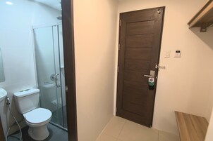 Baño con inodoro, cabina de ducha de vidrio y puerta de madera.