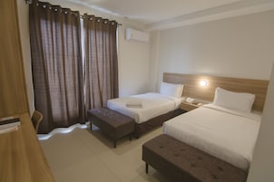 Habitación de hotel con dos camas, un escritorio, una silla y una ventana con cortinas.