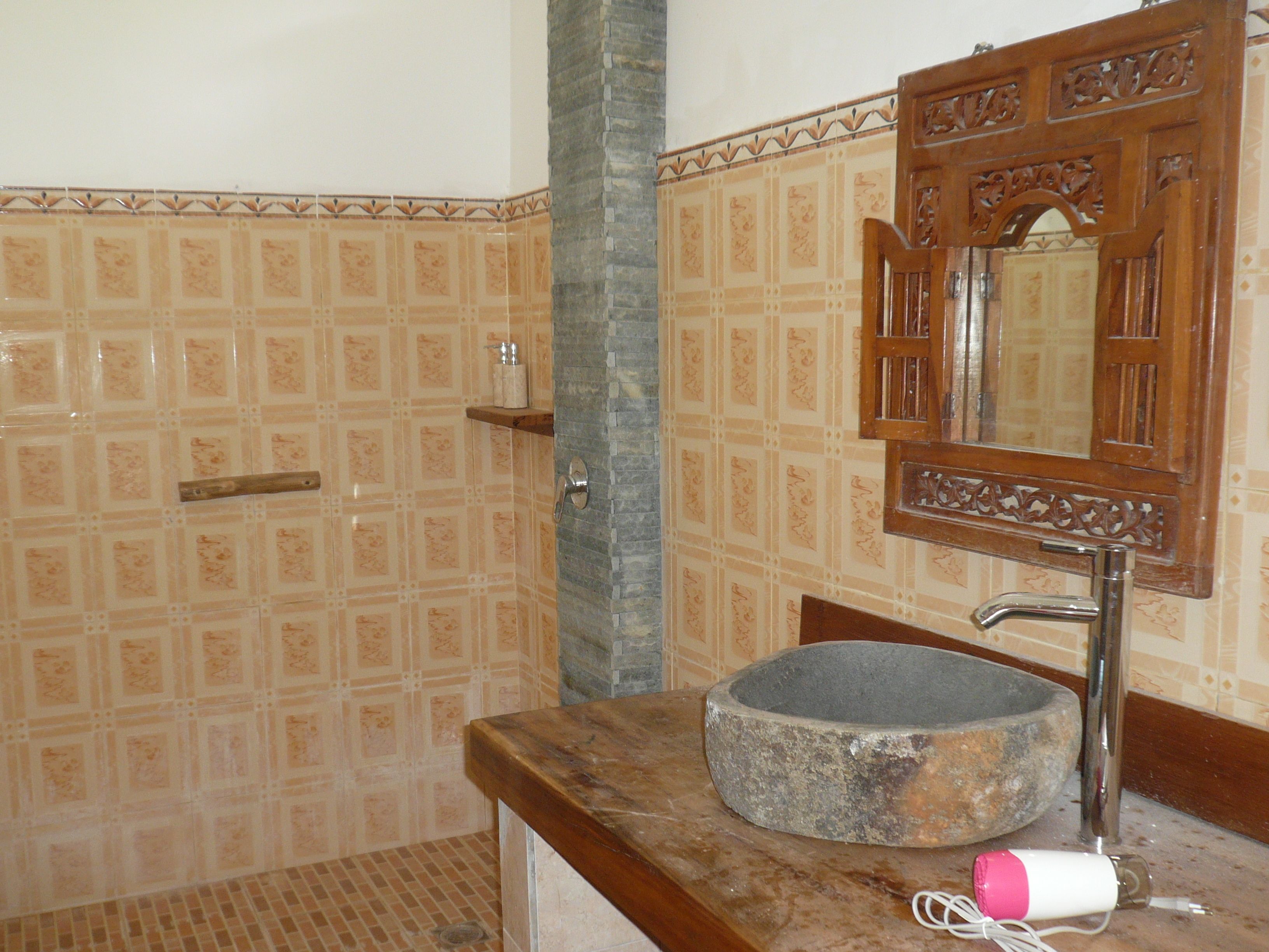 A bathroom with a stone basin, a wooden cabinet, and patterned tiles.