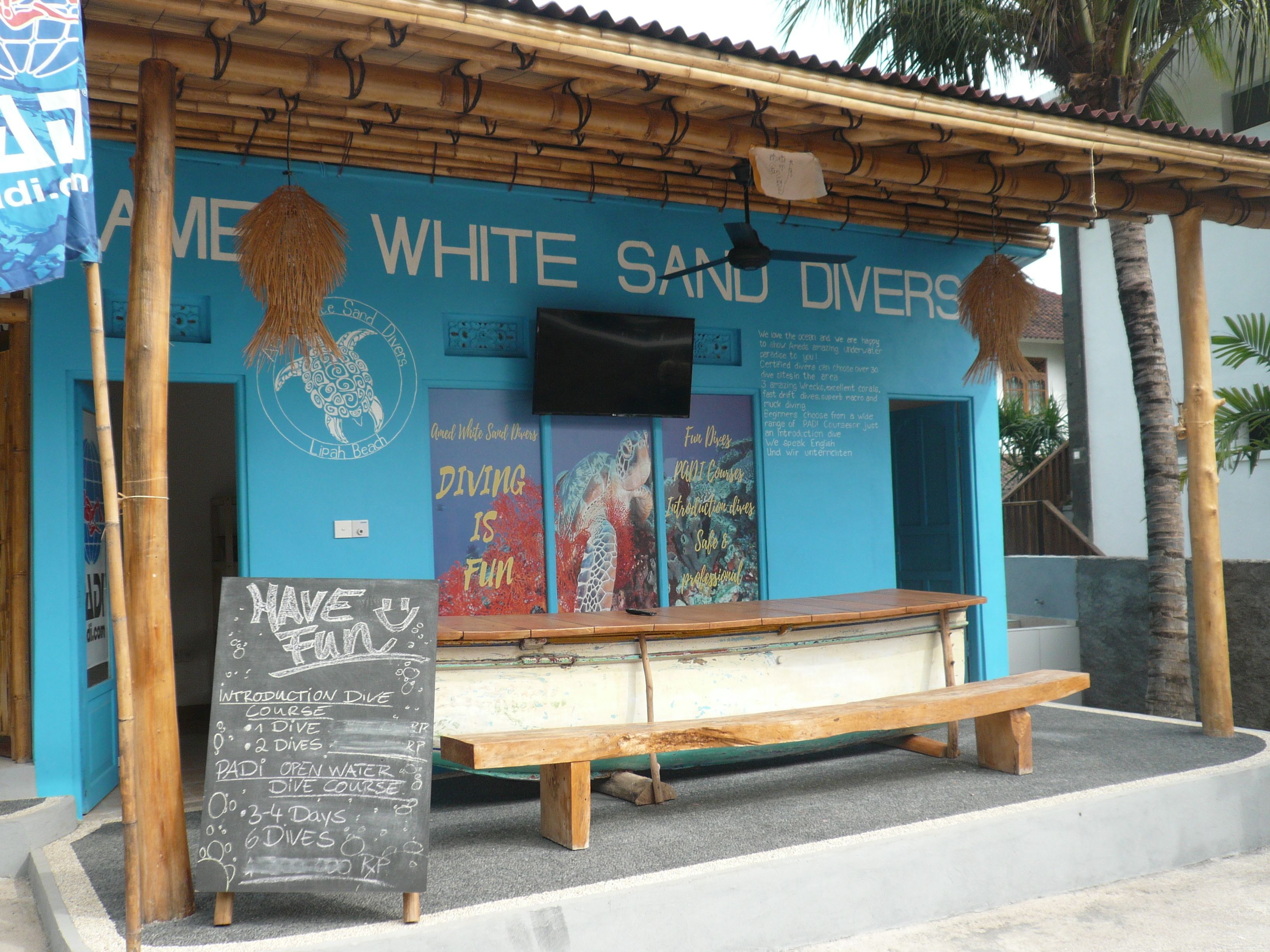 Un centro de buceo frente a la playa, con un banco de madera y una pizarra que anuncia cursos de buceo.