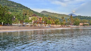Un hotel frente a la playa con varias habitaciones, una piscina y vistas al océano y las colinas.