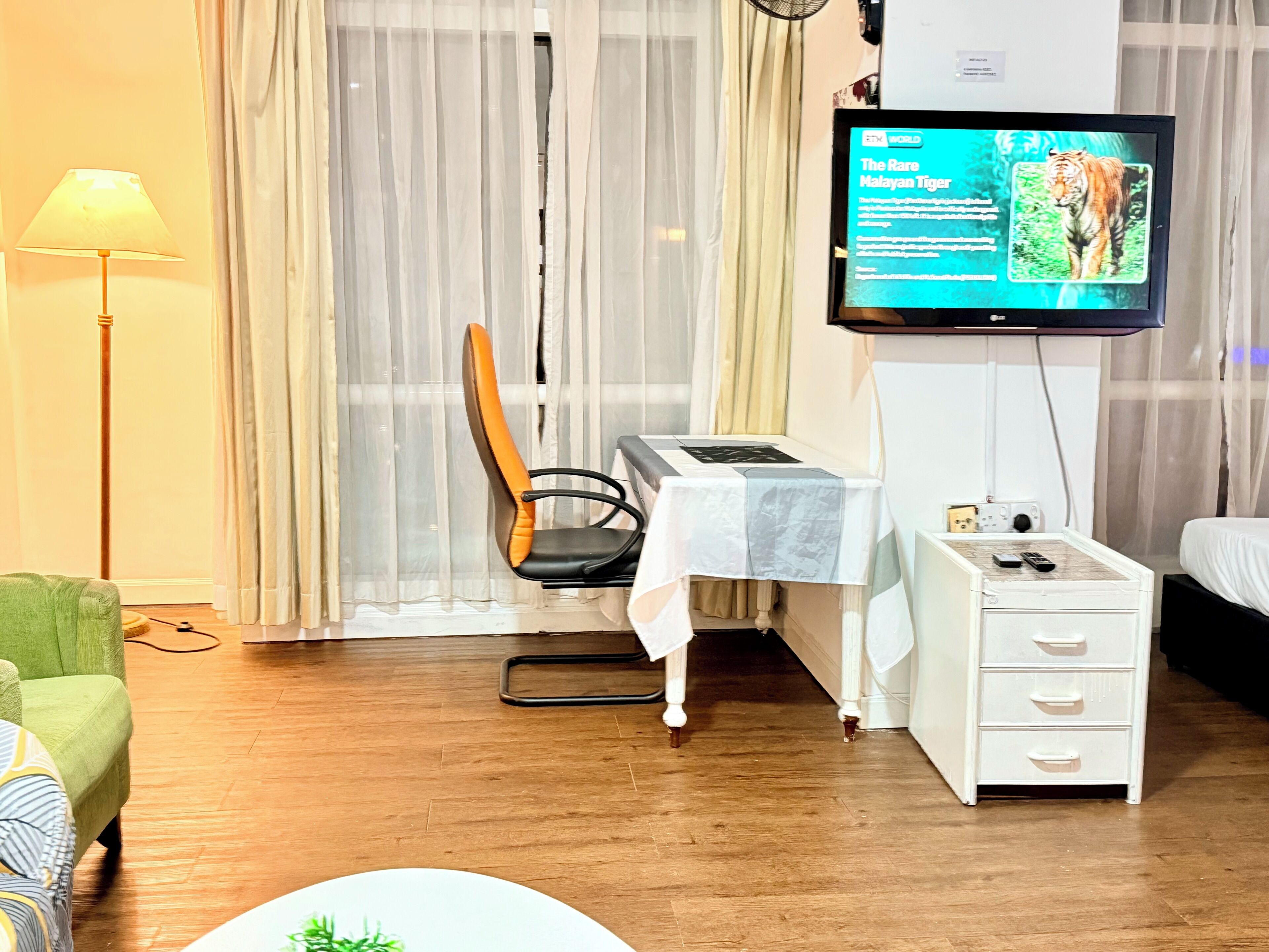 Une chambre d’hôtel comprenant un lit, un bureau avec une chaise, un téléviseur fixé au mur, une lampe et un fauteuil vert.