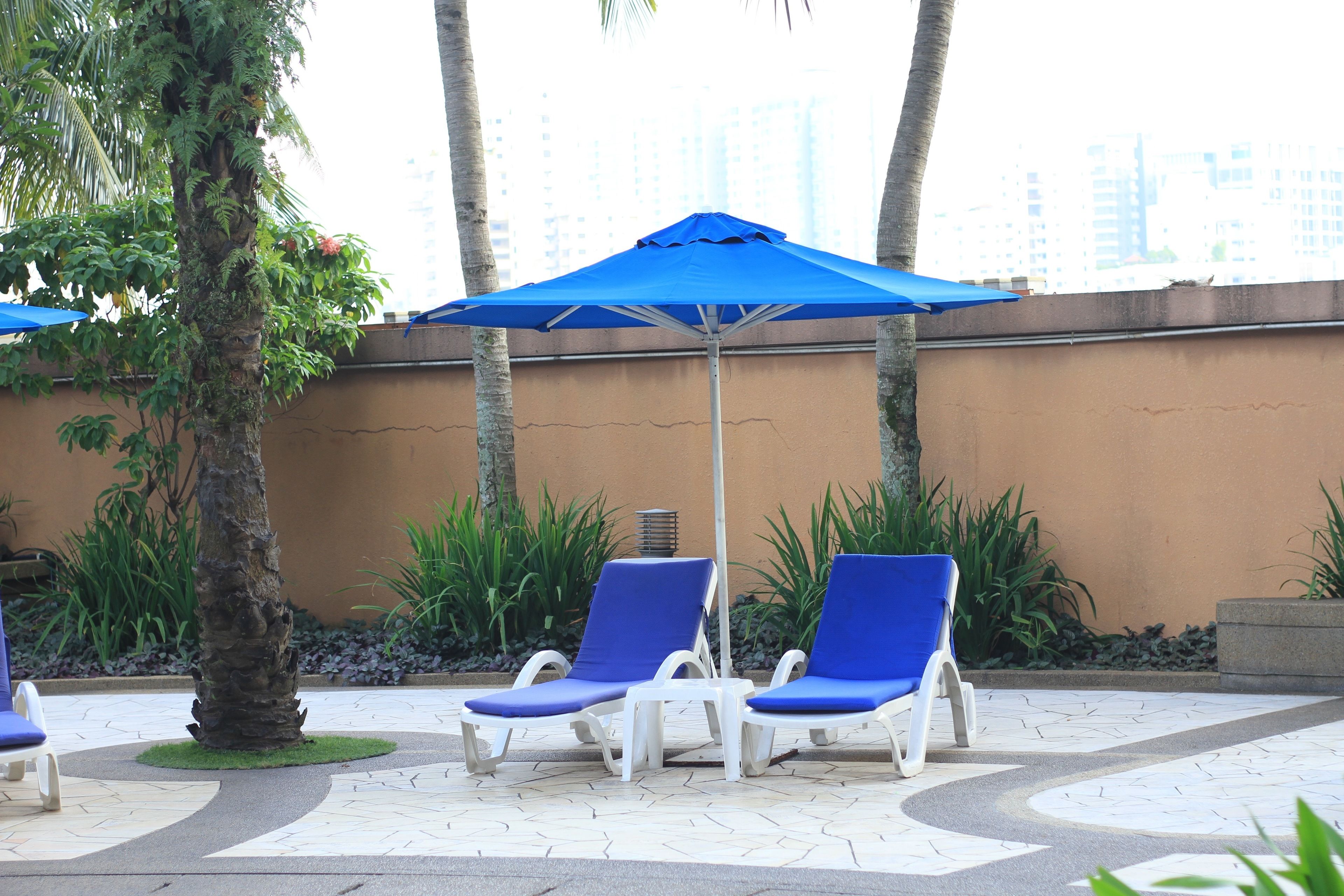 A poolside area with lounge chairs and a blue umbrella.
