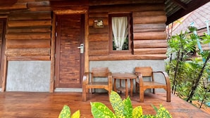 A log cabin with a wooden door, a window with a curtain, and a small table with two chairs outside. - Yotaka Pai (Pai)