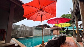 A swimming pool area with a tiled floor, a wooden fence, and outdoor seating. - Yotaka Pai (Pai)