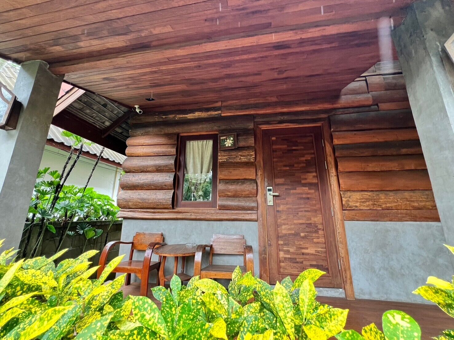 A wooden cabin with a porch, a door, and two small tables with chairs.