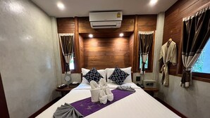 A hotel room with a large bed, wooden paneling, an air conditioning unit, a bedside table with a lamp, a telephone, and a window with curtains. - Yotaka Pai (Pai)