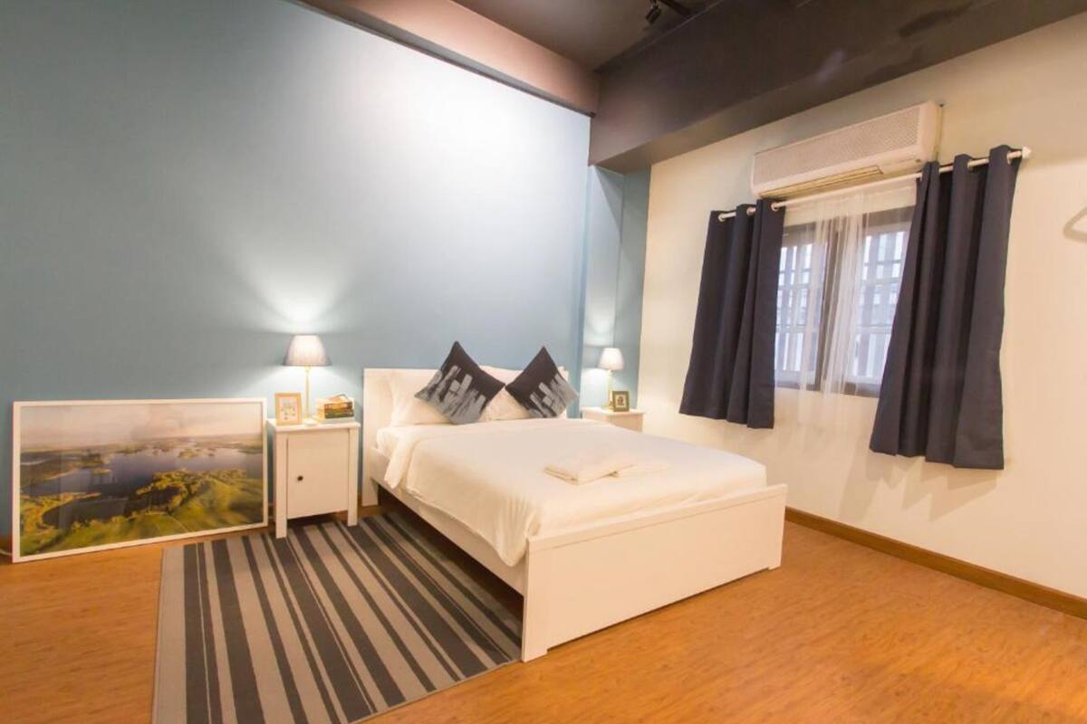 A bedroom with a bed, bedside tables, a nightstand, a painting, and a window with curtains.