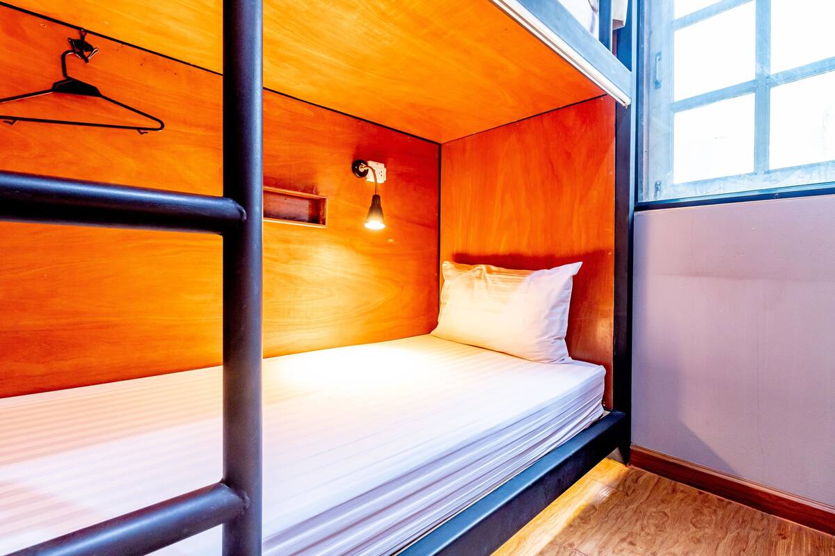 A bunk bed room with wooden walls, a hanging light fixture, and a window.