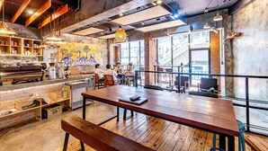 Una cafetería moderna con paredes de ladrillo visto, mesas de madera y lámparas colgantes.