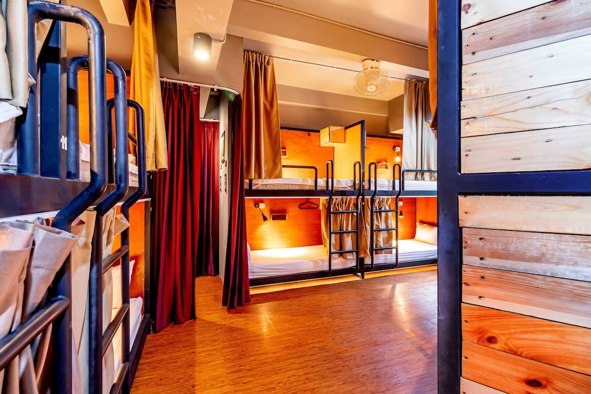 A dormitory room with bunk beds, a wooden floor, and a curtain divider.