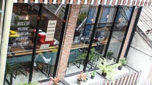 Un hostal con fachada de vidrio, un letrero que indica 'Café ABIERTO' y plantas en macetas en el alféizar.