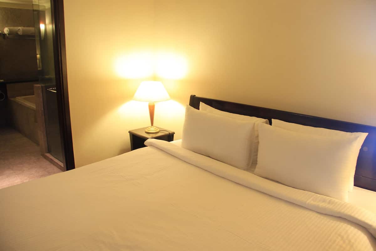 A neatly made bed with white linens and pillows, a bedside lamp, and a nightstand.