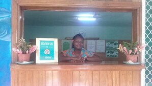 A reception desk with a framed sign that reads "REVIEW US ON advisor.com", two potted plants, and a bulletin board with various notices. - Rekona Lodge (Gizo)
