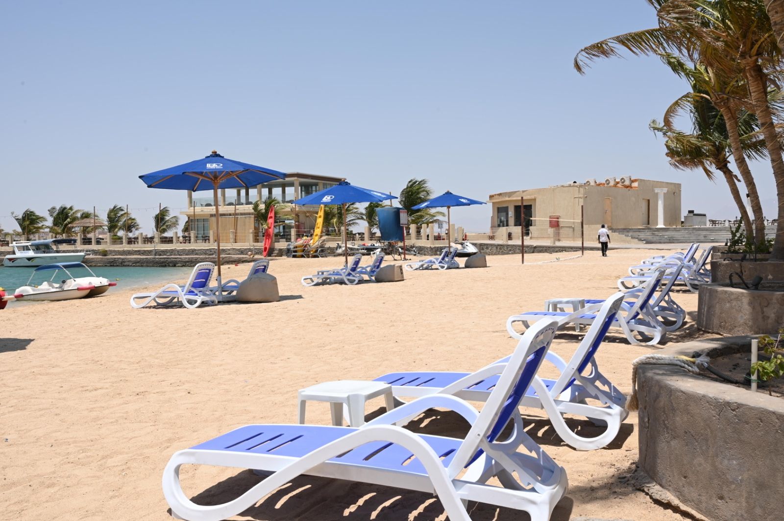 A beach with sun loungers, umbrellas, and a building in the background.