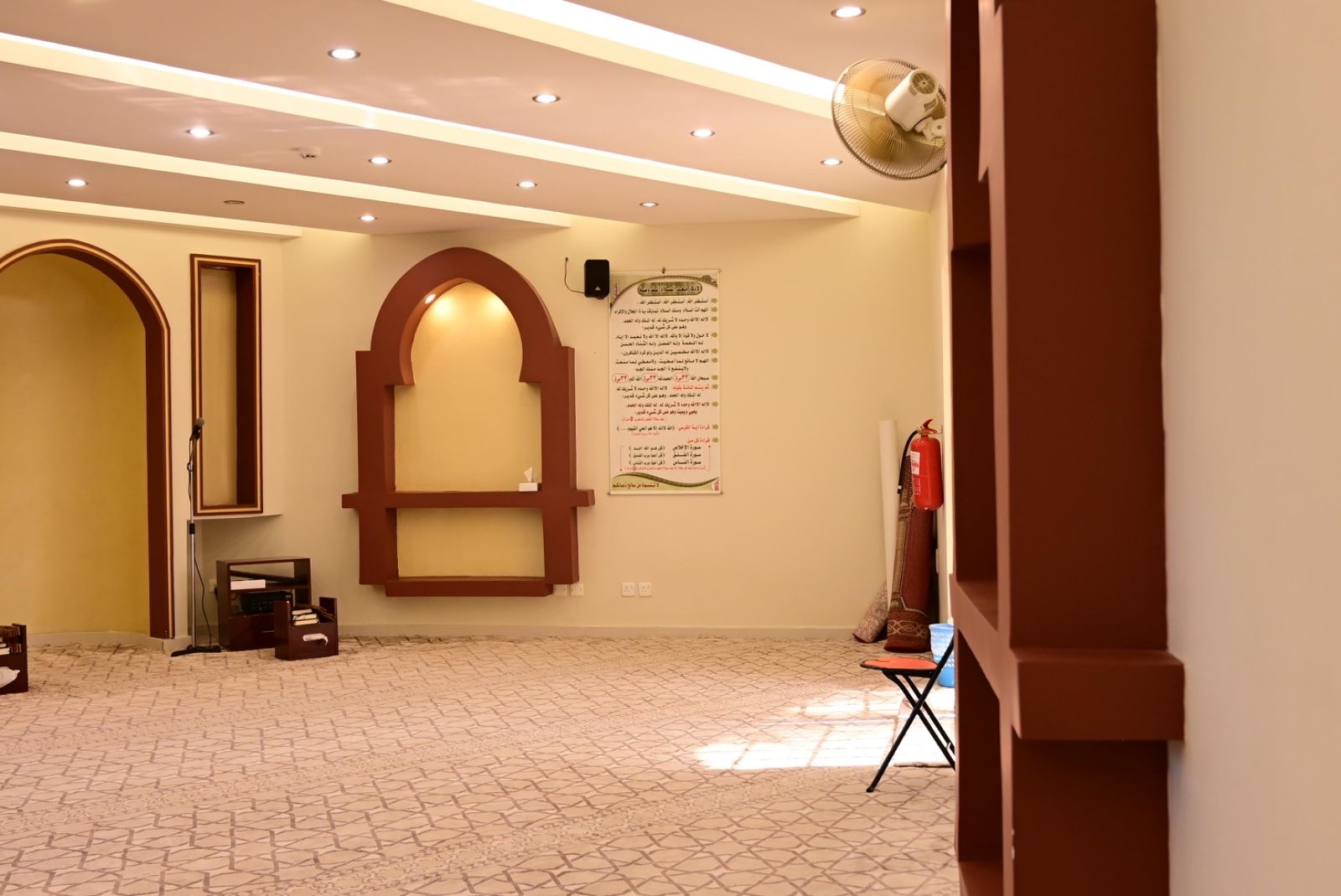 A room with a tiled floor, a large arched doorway, a wall-mounted sign, and a ceiling fan.