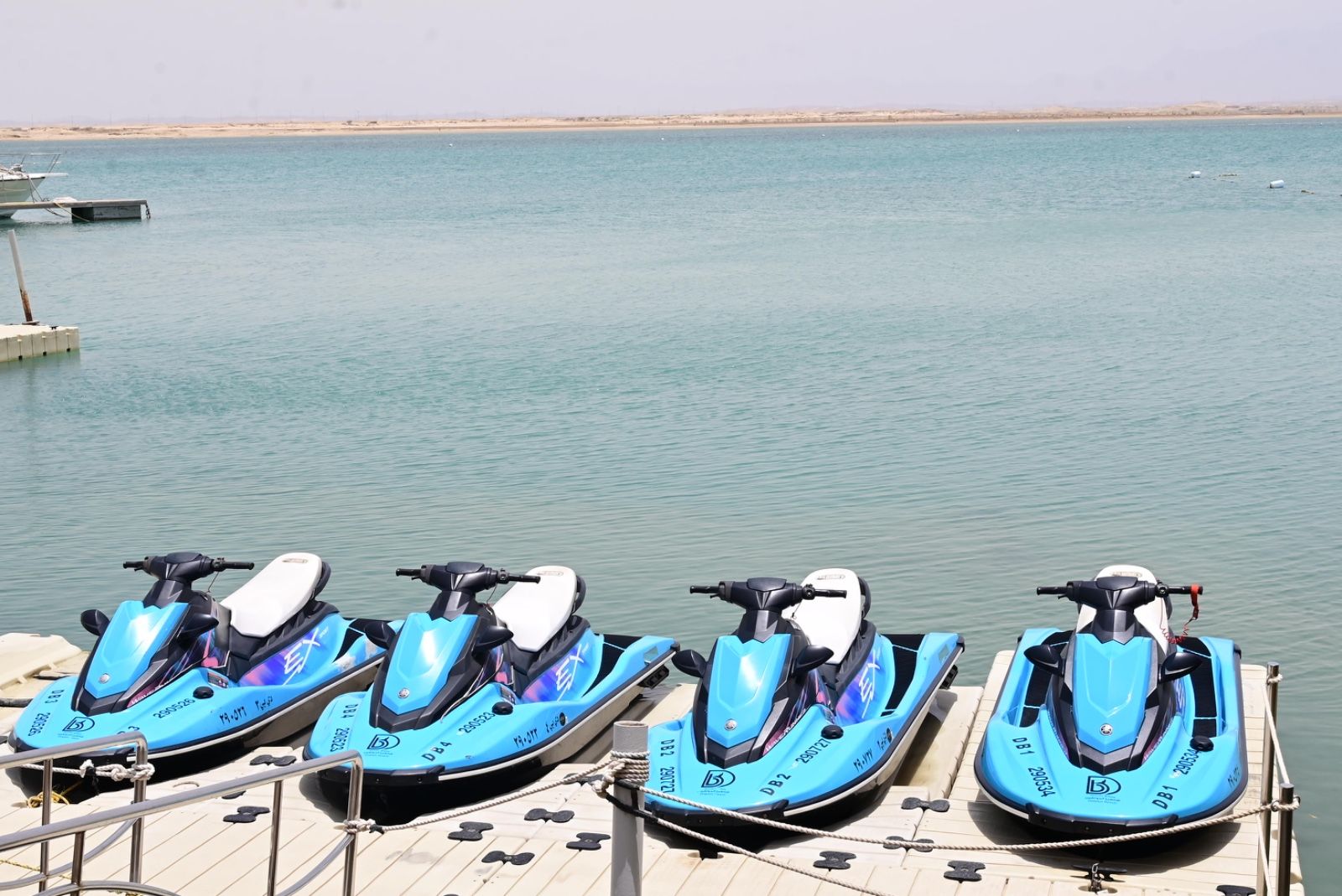 Four jet skis parked on a wooden dock by a calm body of water.