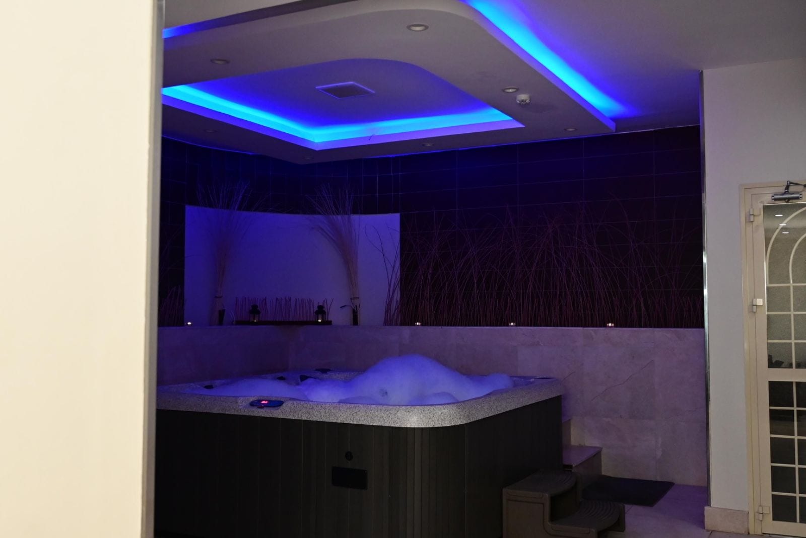 A modern bathroom with a freestanding hot tub, recessed ceiling lighting, and a tiled wall.