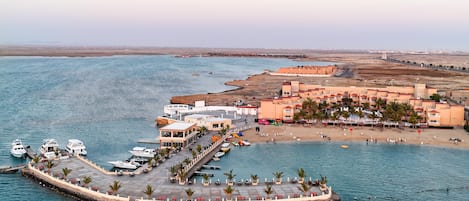 Un complejo turístico frente al mar con un puerto deportivo, playa y una pequeña isla con muelle.